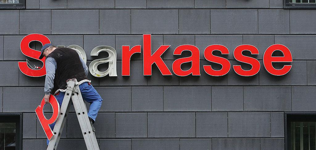 En arbetare reparerar Sparkassebankens skylt i Berlin. Tyskarna sparar i större grad kontanter i sina egna hem.  (Foto: Sean Gallup/Getty Images)