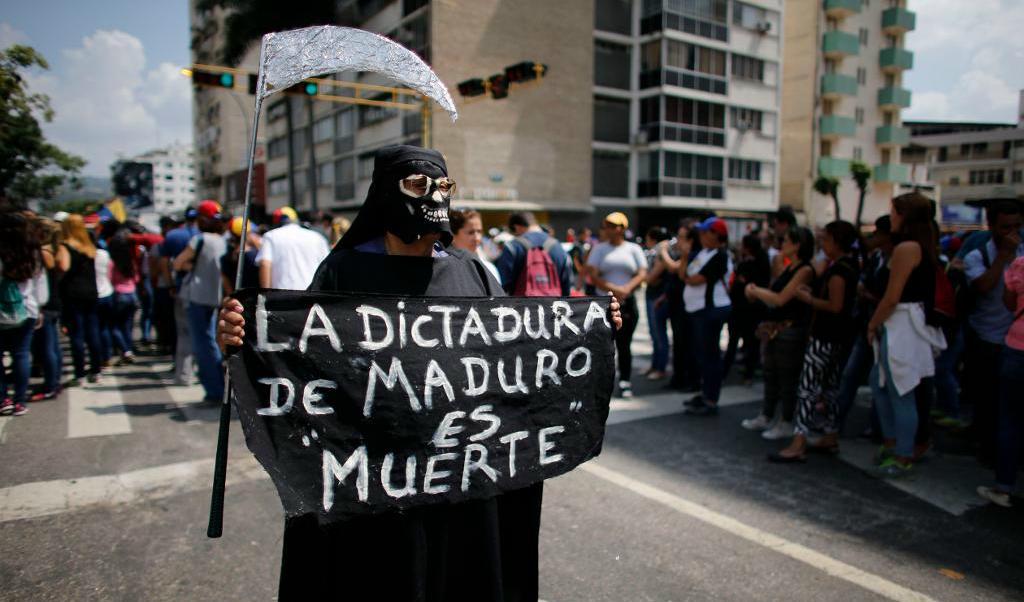 
"Maduros diktatur är döden", står det på den här kvinnans skylt, vilket anspelar på en oppositionell demonstrant som dödades i veckan. Foto: Ariana Cubillos/AP/TT                                            
