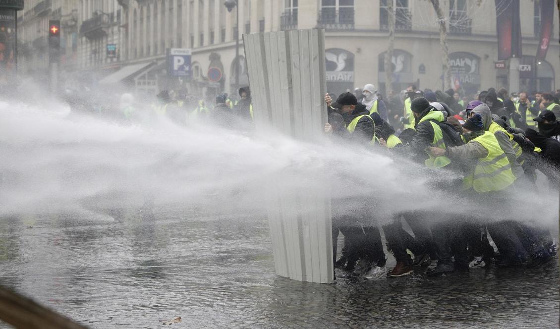 Polis använder vattenkanoner mot demonstranter i Paris. Foto: Kamil Zihnioglu/AP/TT