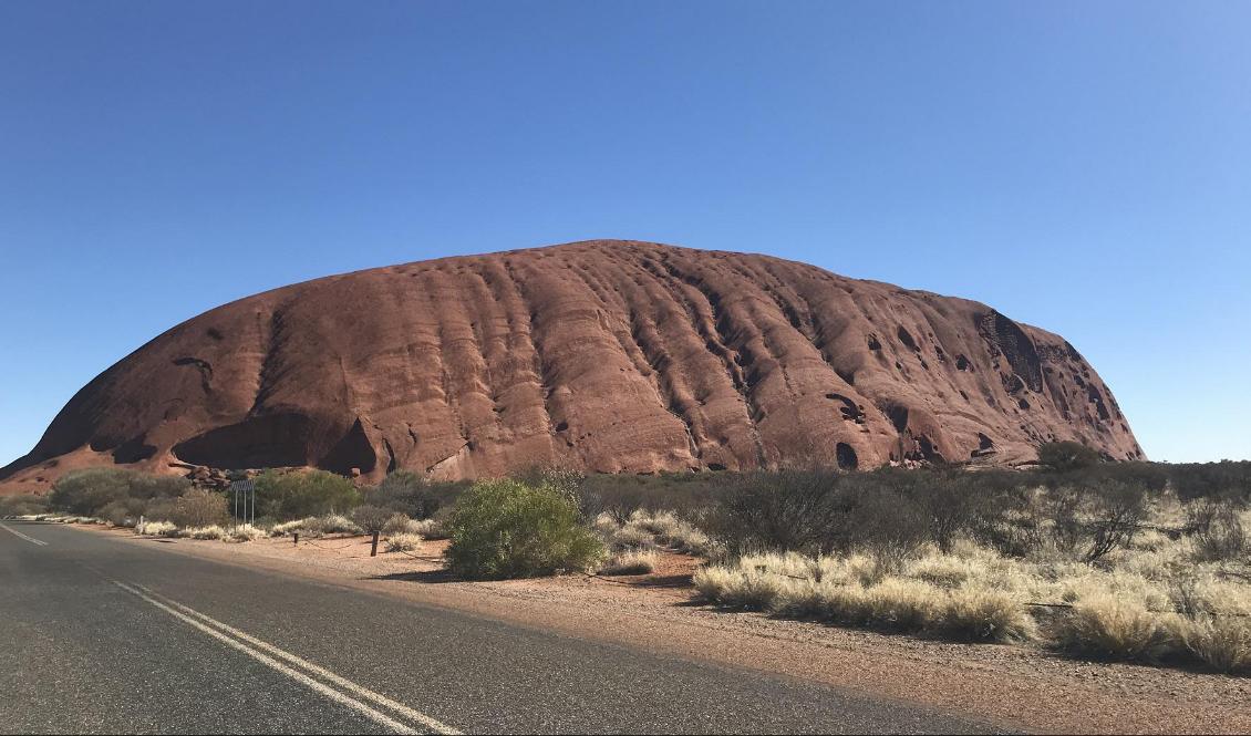 För den som närmar sig med bil tornar klippan upp sig på långt håll. Spåren på berget har enligt aboriginernas berättelser bildats när ödle- och ormvarelser krigade.  Foto: Henrik Samuelsson/TT