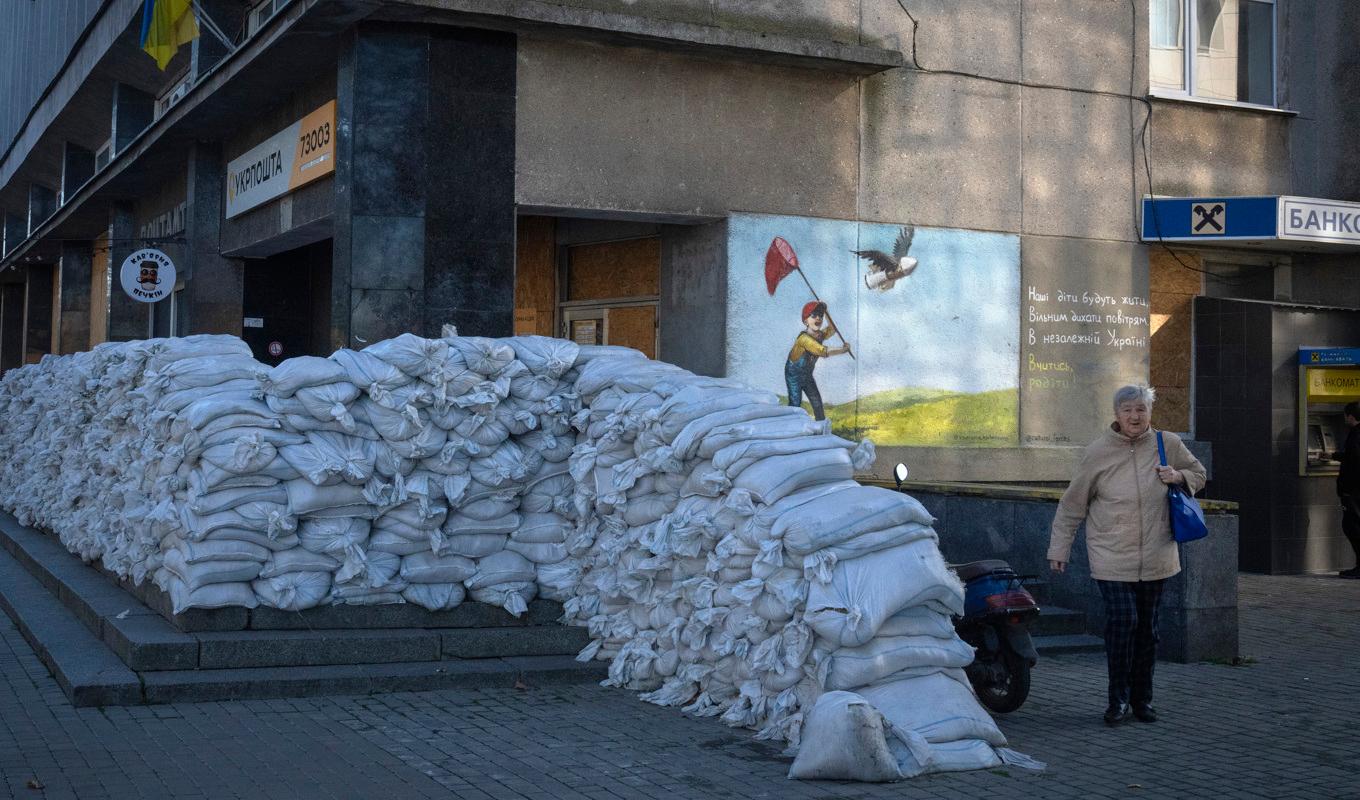En invånare i staden Cherson promenerar förbi en mur av sandsäckar som byggts för att skydda ett postkontor. Bilden togs den 10 november. Foto: Efrem Lukatsky/AP/TT