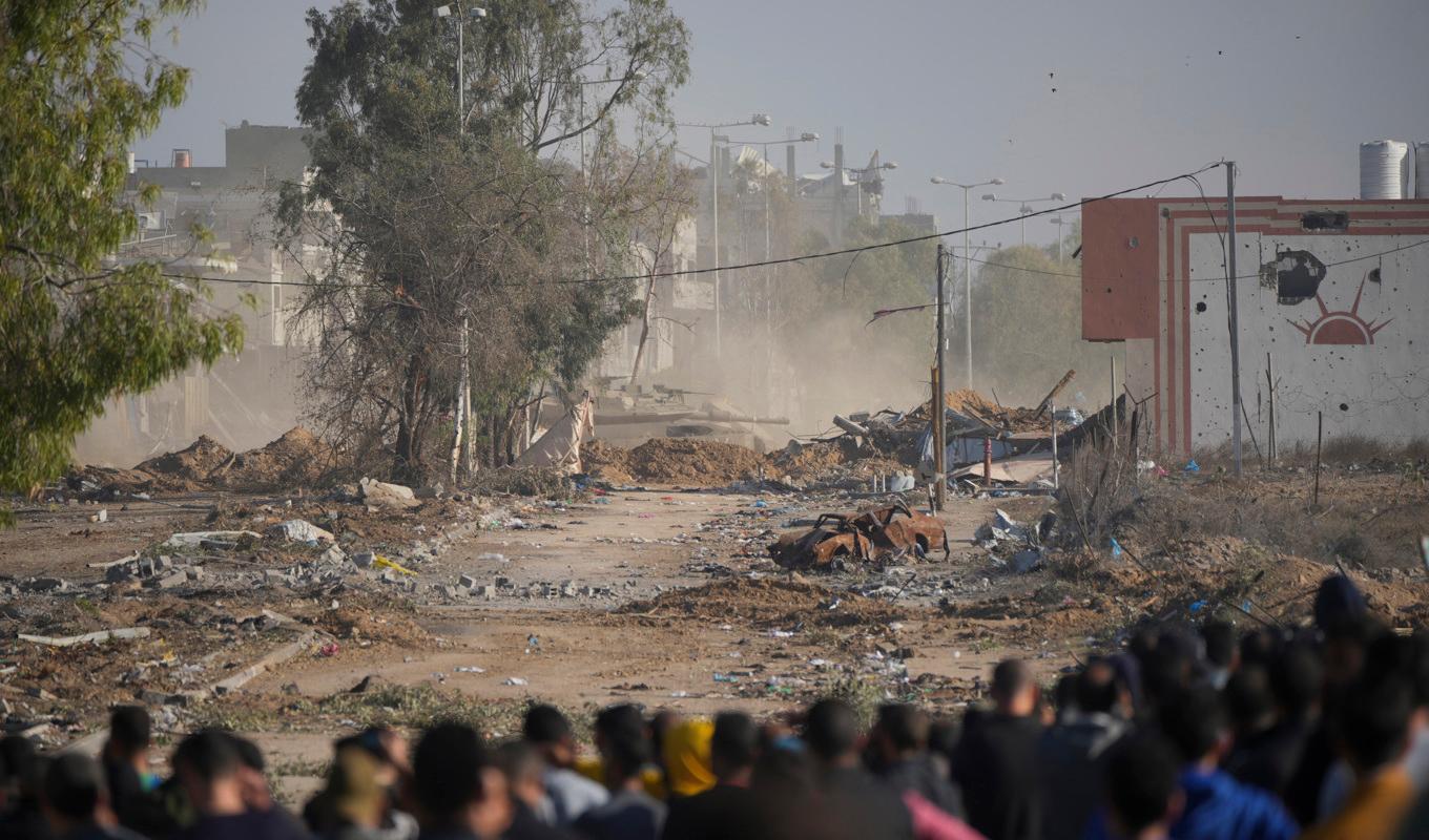Palestinier tittar bort mot en israelisk stridsvagn som på fredagen blockerar Saladinvägen, den enda större genomfartsleden mellan södra och norra Gazaremsan. Foto: Hatim Mussa/AP/TT