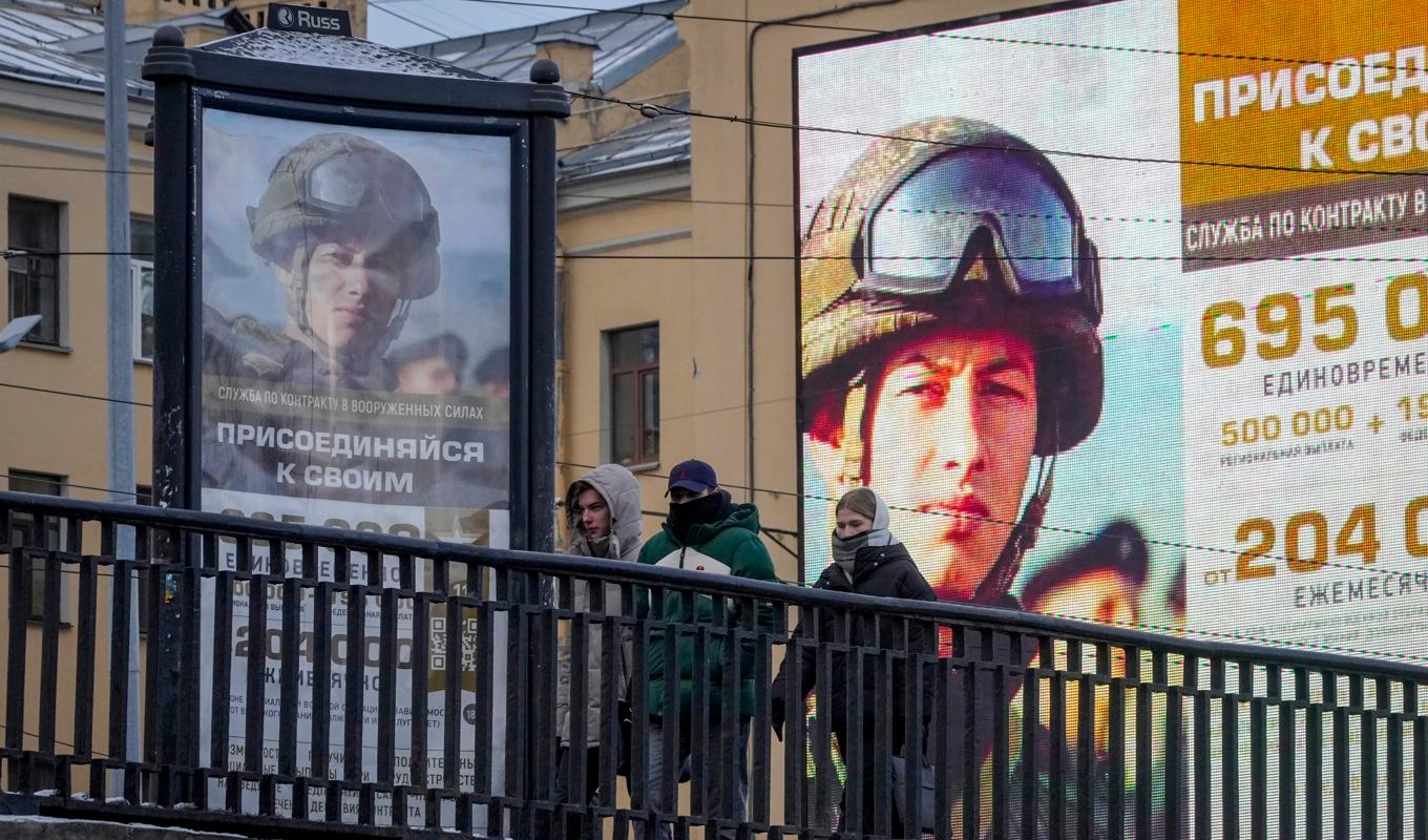 Några unga personer i S:t Petersburg promenerar förbi reklamtavlor där de uppmanas ta värvning i armén. Bilden togs den 22 november. Foto: Dmitri Lovetsky/AP/TT