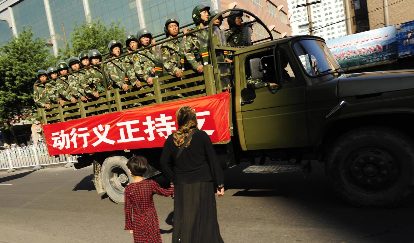 På bilden ses en kvinna och hennes dotter korsa vägen när kinesisk paramilitärpolis kör förbi Urumqi i Xinjiangregionen den 9 juli 2009. Foto: Peter Parks/AFP via Getty Images