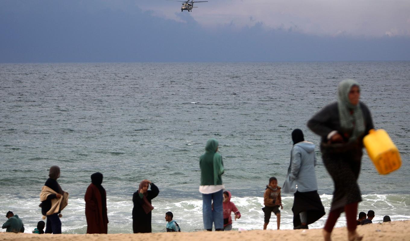 Oroliga palestinier på stranden utanför Khan Yunis tittar ut mot en israelisk militärhelikopter som patrullerar Medelhavet. Bild från i förra veckan. Foto: Mohammad Dahman/AP/TT