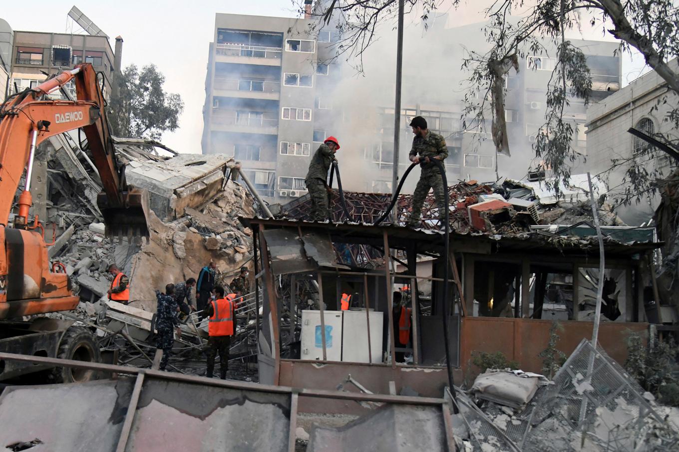 Personal vid rasmassorna efter flygräden mot Irans konsulat i Damaskus. Foto: Sana via AP/TT