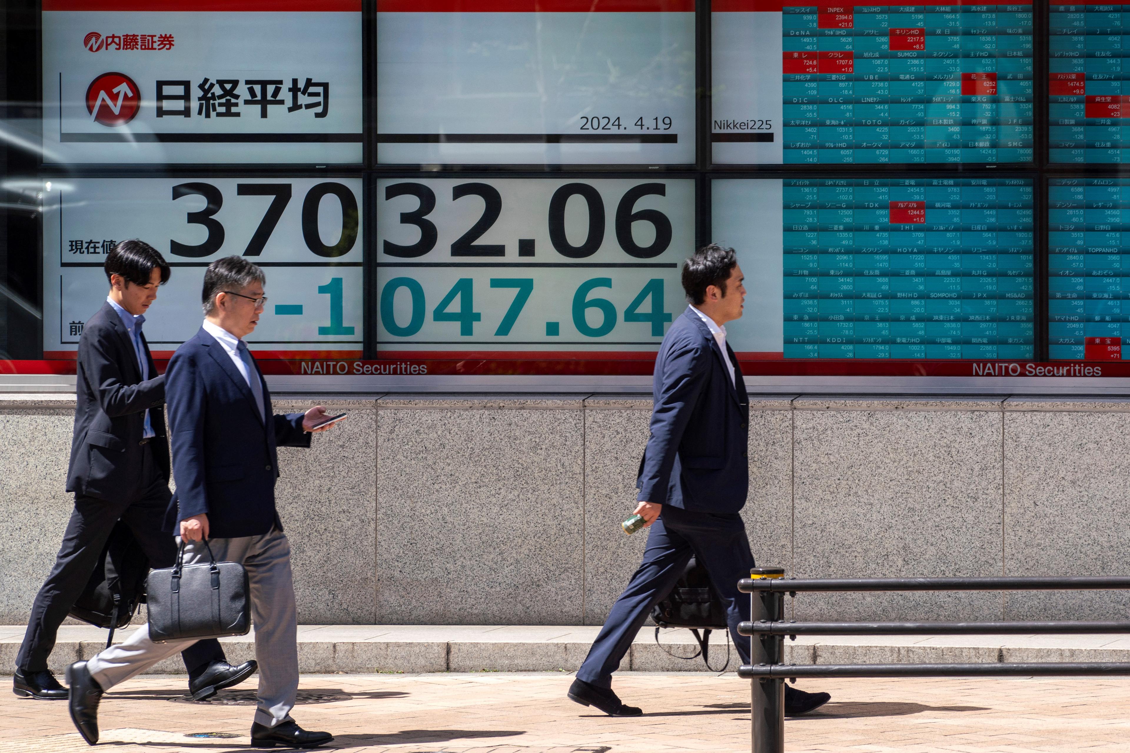 Fotgängare går framför en elektronisk tavla som visar aktiekursen för Nikkei-indexet på Tokyobörsen längs en gata i Tokyo den 19 april. Foto: Kazuhiro Nogi/AFP via Getty Images