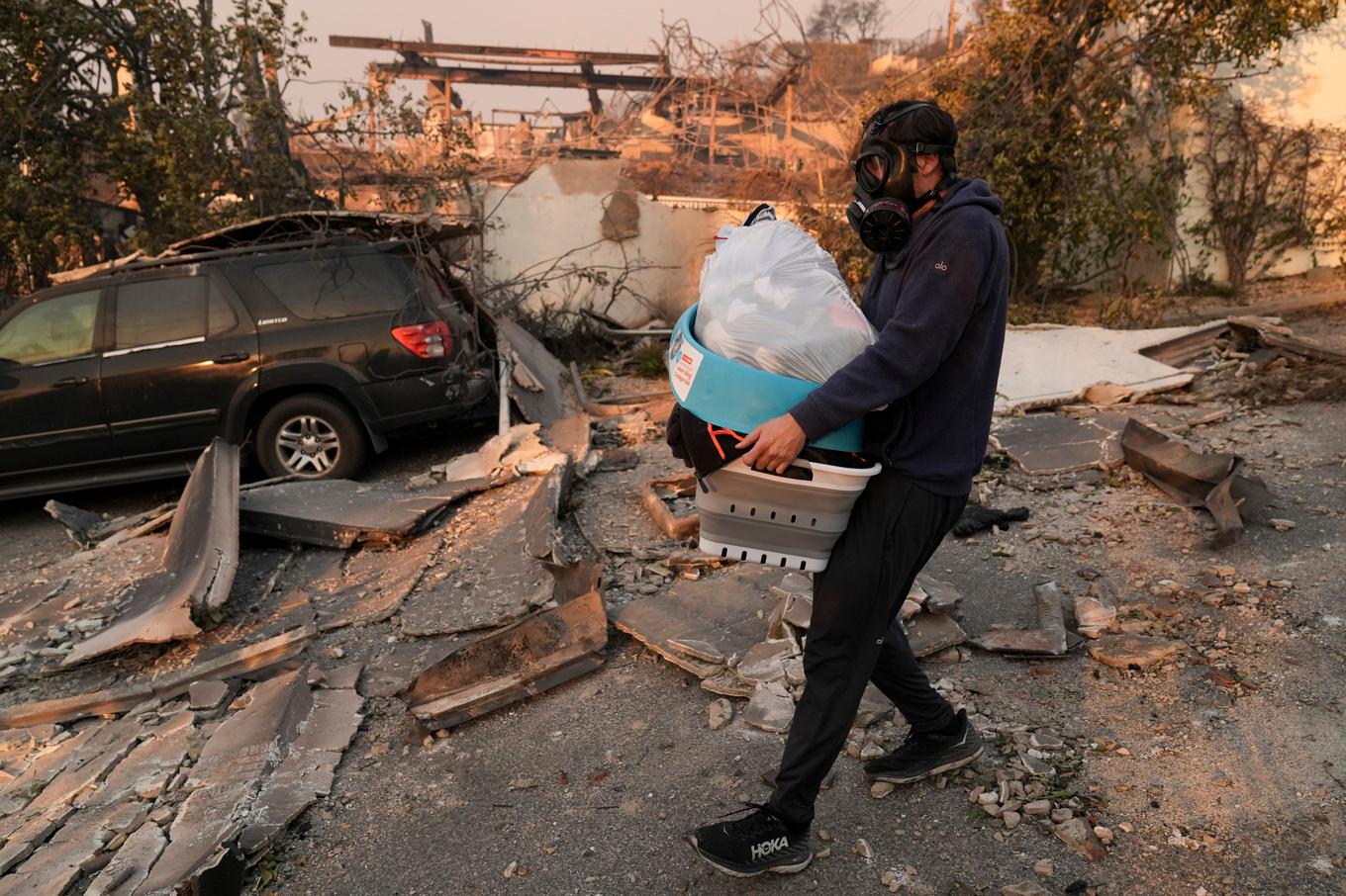 En man bär på sina barns kläder som han fått med sig från sitt eldhärjade hem i Pacific Palisades i Los Angeles. Foto: Jae C. Hong/AP/TT
