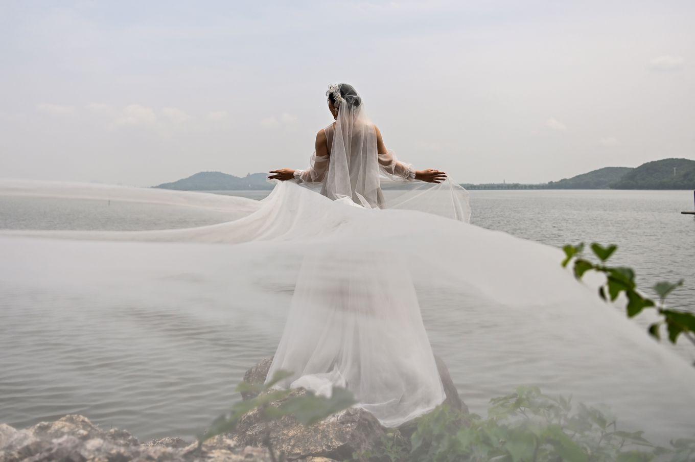 En brud i bröllopsklänning poserar för bröllopsfotografen vid Östra sjön i staden Wuhan i Hebeiprovinsen i centrala Kina, den 16 maj 2020. Foto: Hector Retamal/AFP via Getty Images