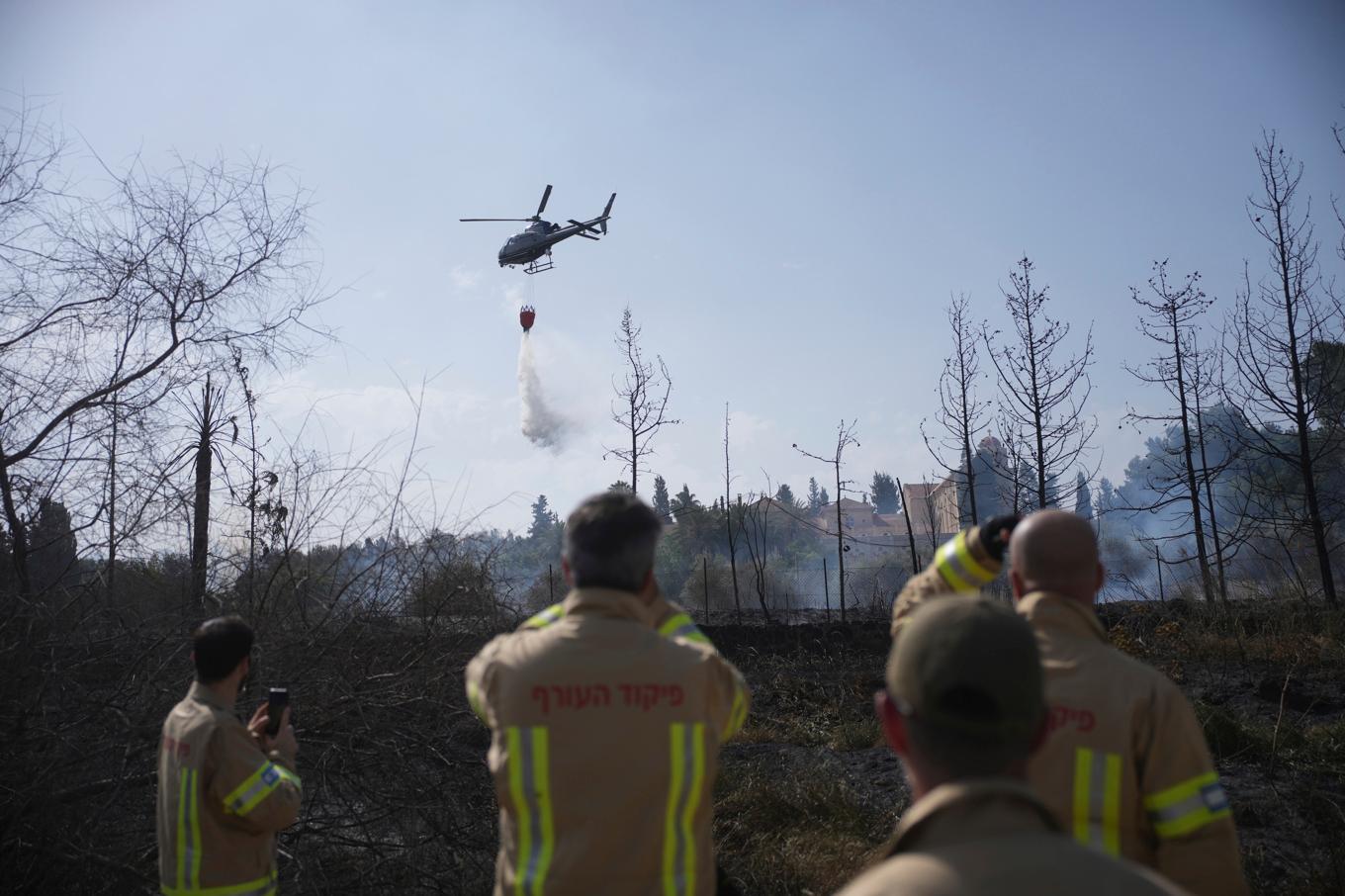Israeliska brandmän ser på när en helikopter släpper vatten över bränderna. Foto: Ohad Zwigenberg/AP/TT