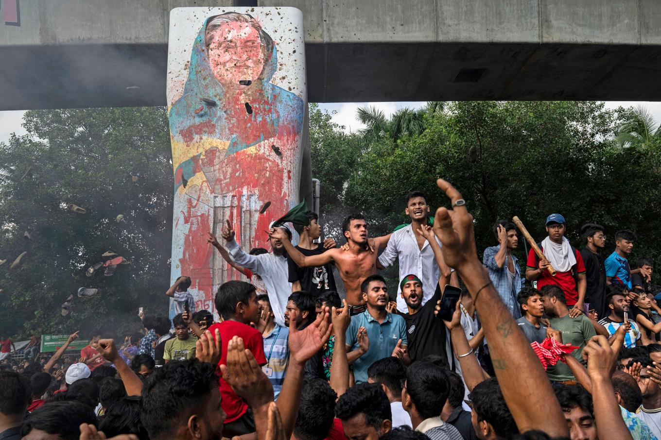 Människor firar att Sheikh Hasina meddelat sin avgång intill ett vandaliserat porträtt av premiärministern. Bild från den 5 augusti 2024. Foto: Fatima Tuj Johora/AP/TT