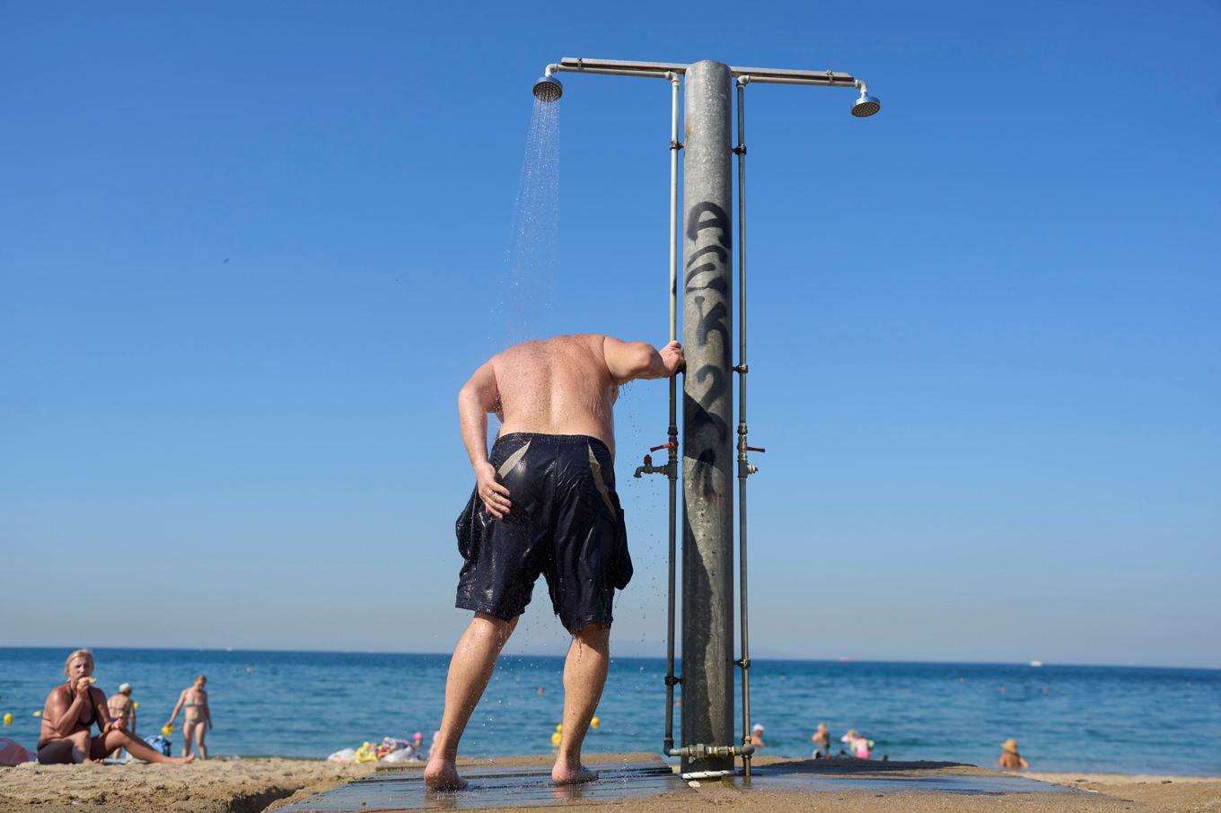 En man tar en dusch på en strand i Greklands huvudstad Aten på torsdagen. Grekland är ett av de länder där man räknar med höga temperaturer i helgen. Foto: Petros Giannakouris/AP/TT