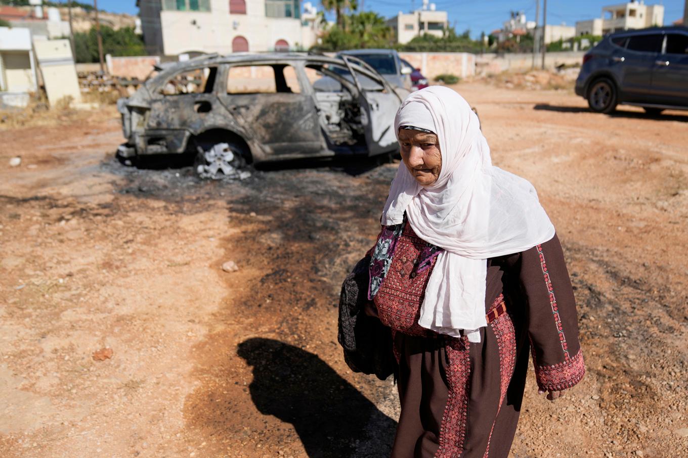 En palestinsk kvinna som går förbi en utbränd bil i den palestinska byn Kafr Malik. Foto: Nasser Nasser/AP/TT
