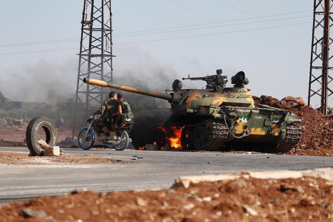 Syriska soldater på en motorcykel passerar en brinnande stridsvagn i utkanten av staden Sweida i södra Syrien, där druser och beduiner drabbat samman. Foto: Omar Sanadiki/AP/TT