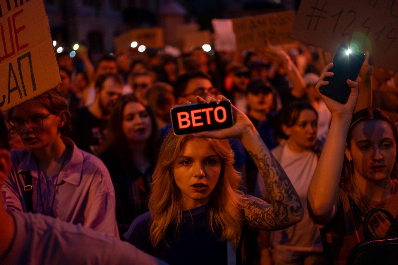 En kvinna håller upp en telefon med ordet "veto" skrivet över skärmen under demonstrationer i Ukrainas huvudstad Kiev mot lagändringen på tisdagskvällen. Foto: Alex Babenko/AP/TT