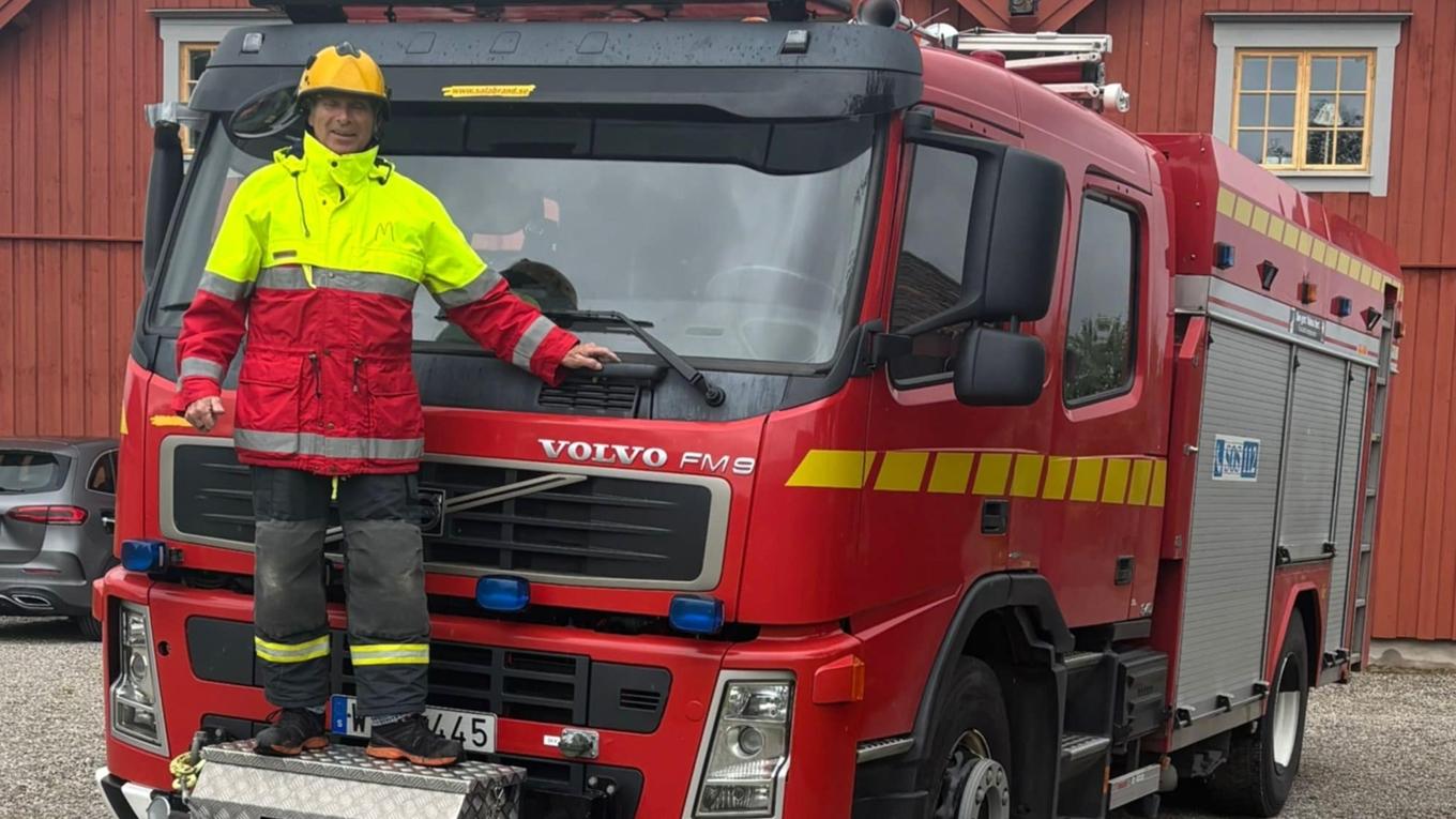 Tage Perntz stående på brandbilen som körs ned till fronten. Fotograf: Roger Sahlström.