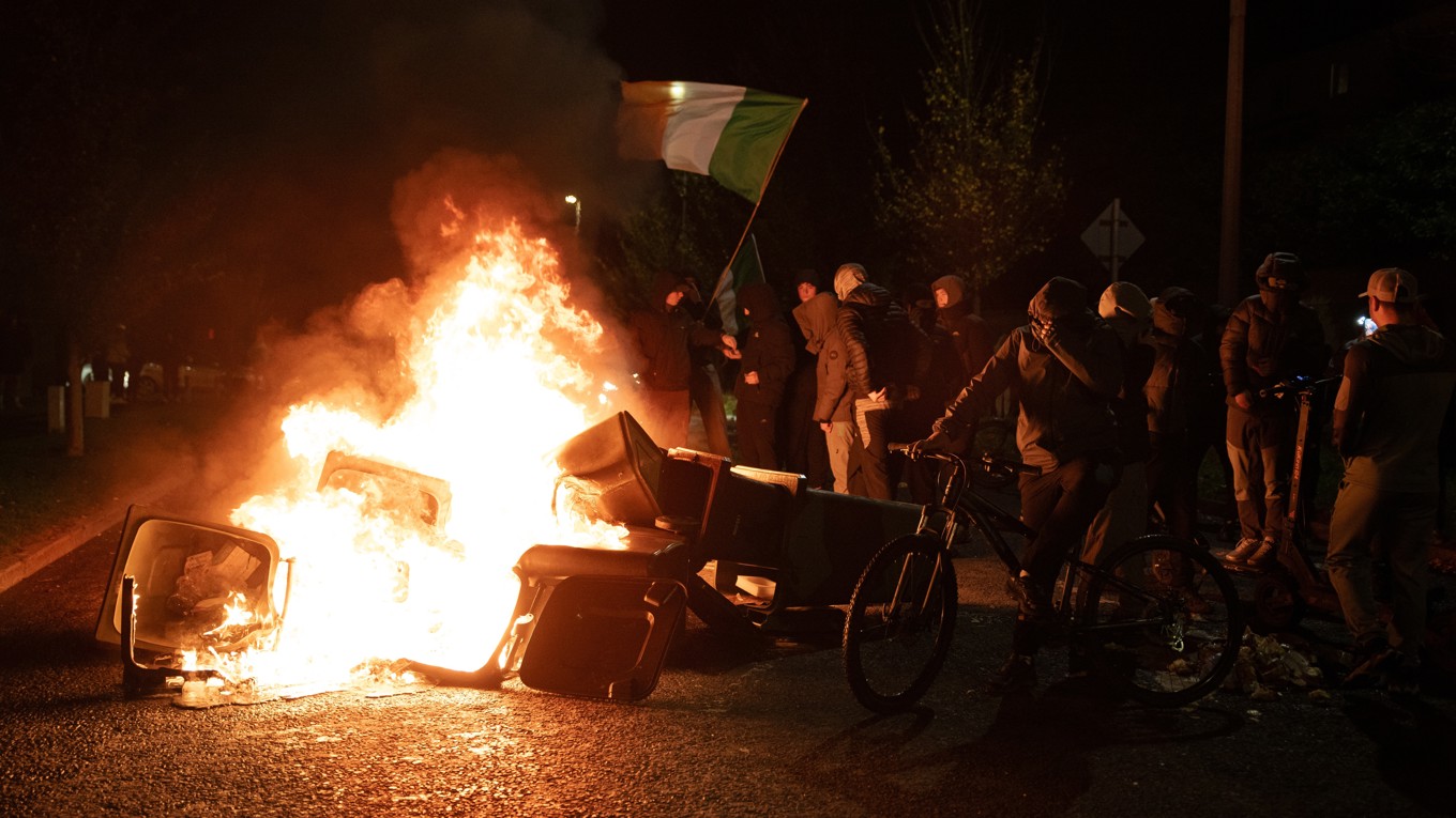 Demonstranter viftar med irländska flaggor bredvid brinnande soptunnor den 21 oktober i irländska Dublin. Foto: Natalia Campos/Getty Images