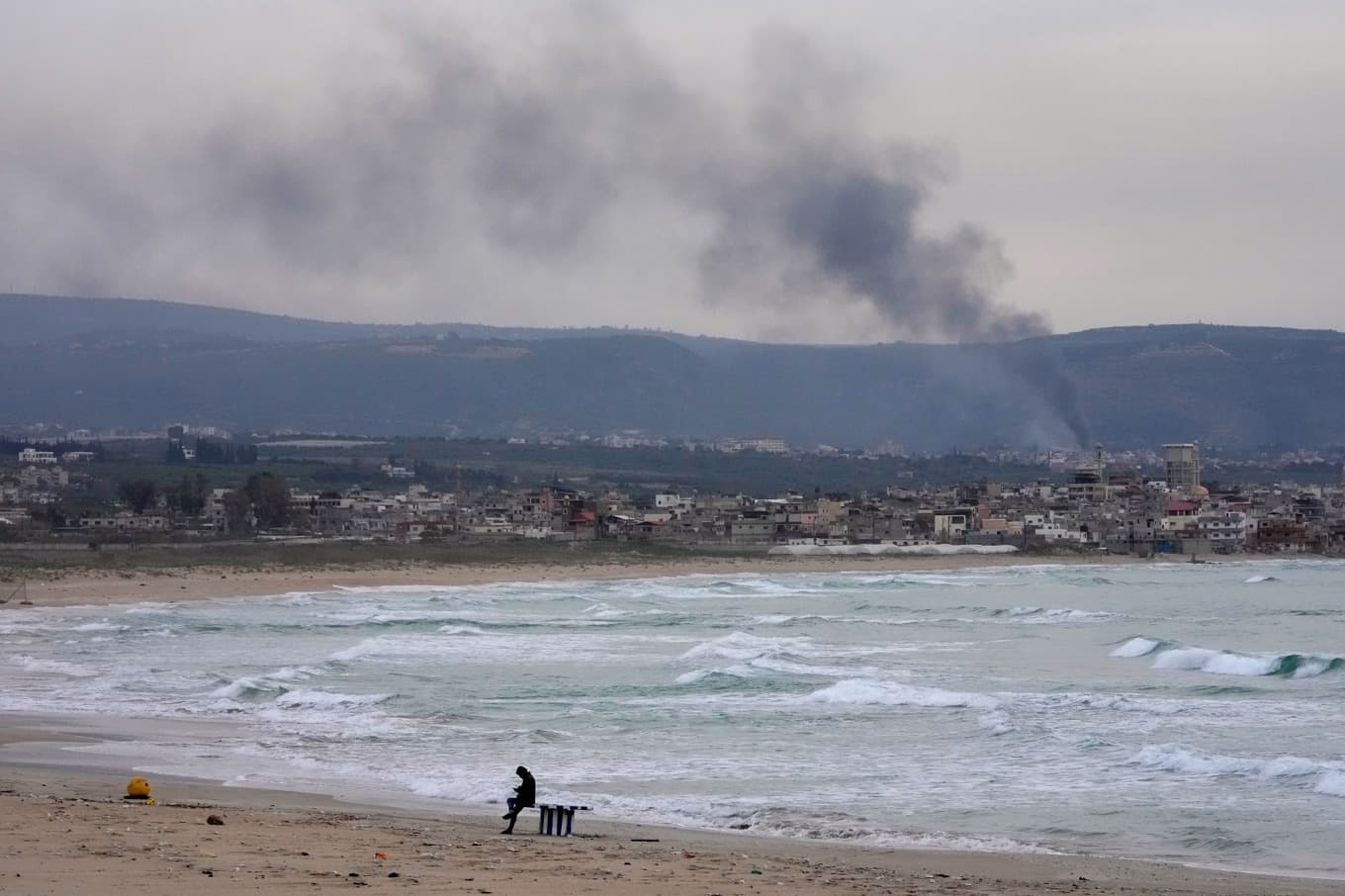 En man syns på stranden medan rök stiger efter en israelisk attack i en by i södra Libanon i lördags. Foto:  Hussein Malla/AP/TT