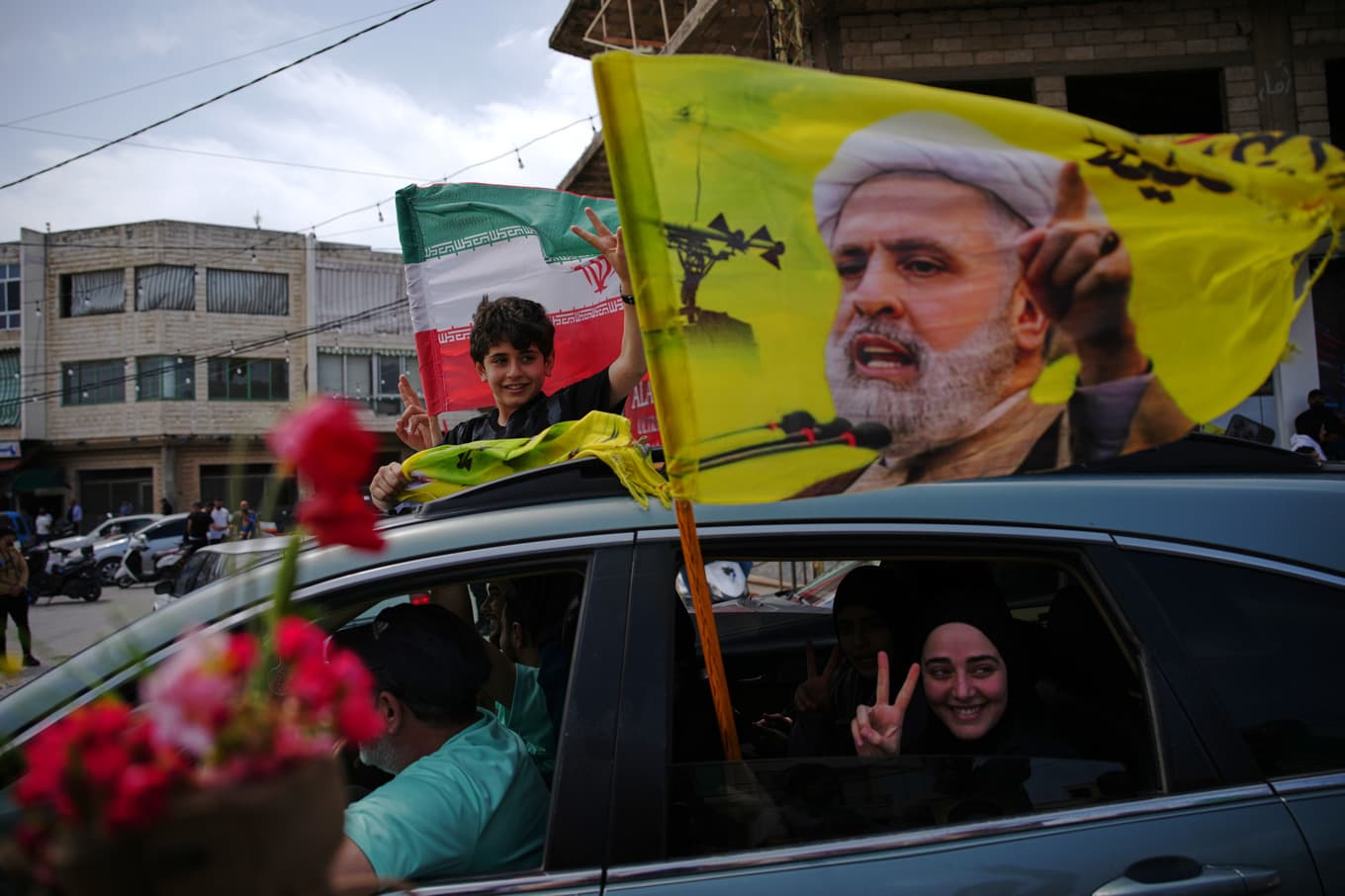 Internflyktingar i Libanon håller upp en flagga med Hizbollahledaren Naim Qassem. Bild från Zefta i södra Libanon i mitten av april. Foto: Hassan Ammar/AP/TT