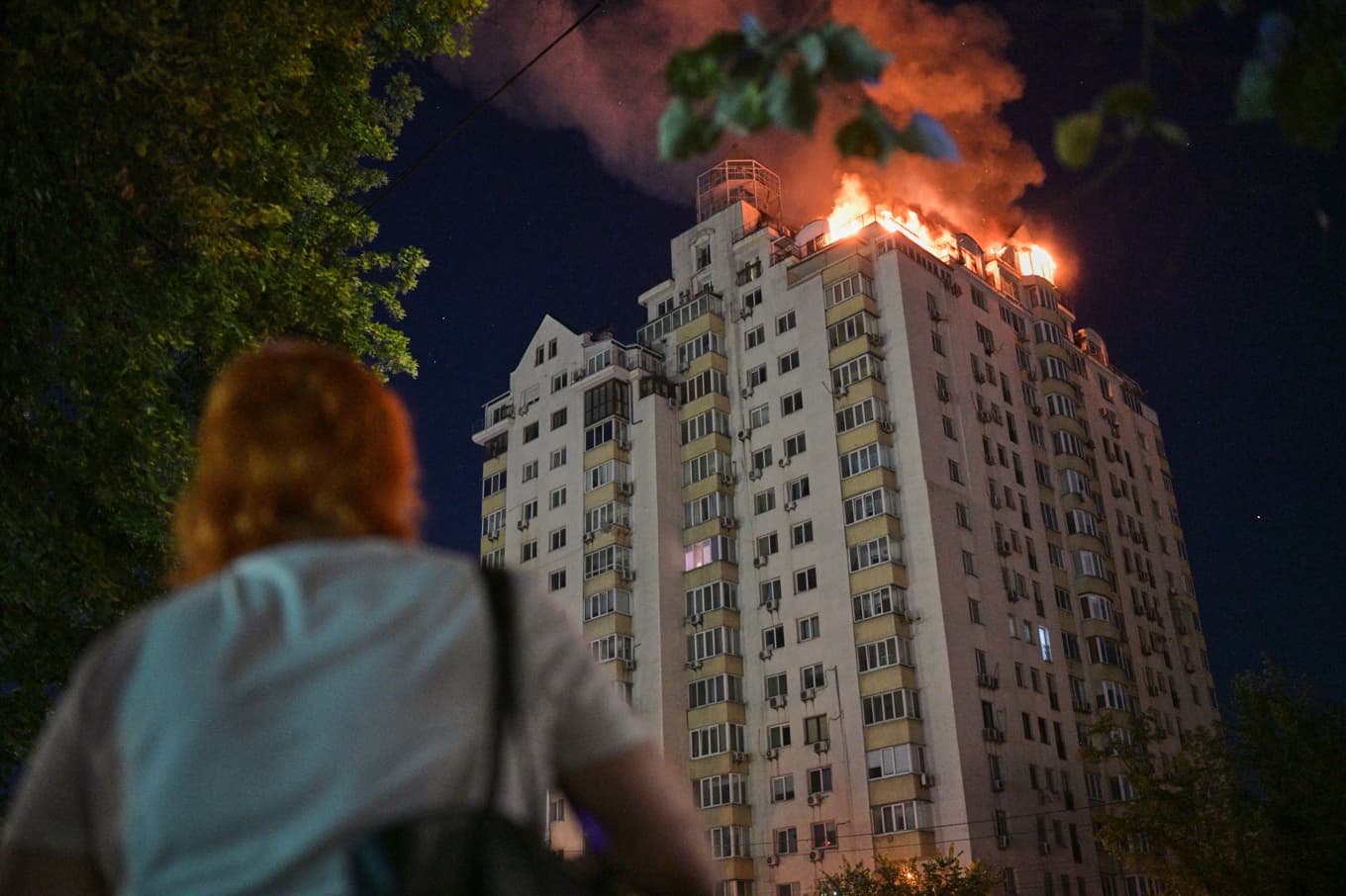 En kvinna framför ett lägenhetshus som stod i lågor under natten. Foto: Danylo Antoniuk/AP/TT