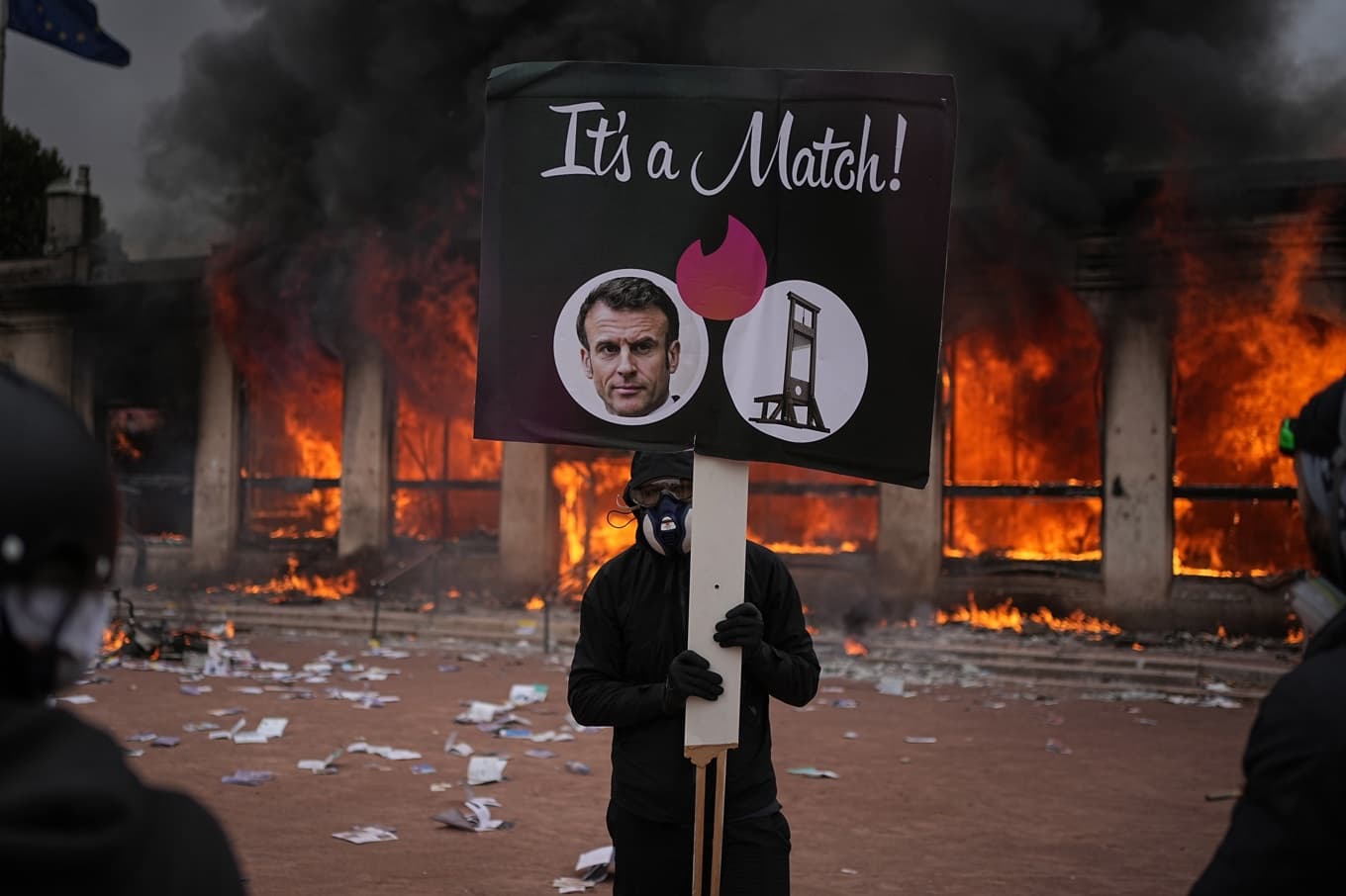 En demonstrant i Lyon i lördags. Plakatet är inspirerat av dejtingappen Tinder – där president Macron ”matchar” med en giljotin. I bakgrunden står en turistbyrå i brand. Foto: Laurent Cipriani/AP/TT