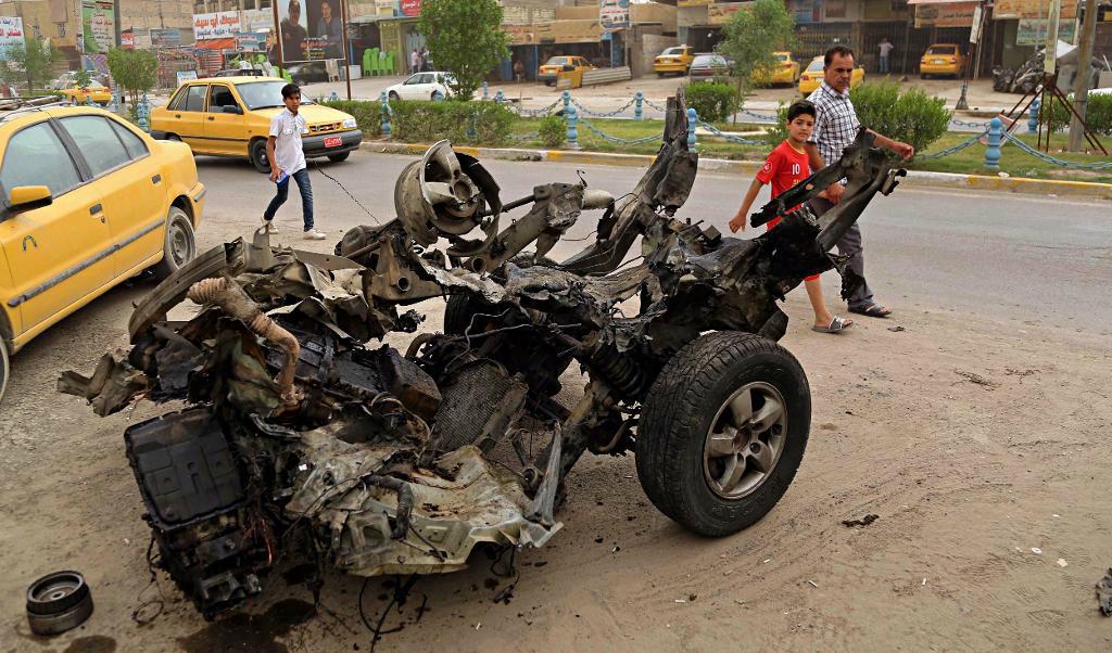 Människor passerar förbi bilvraket efter en självmordsbombning i Bagdad på fredagen. Foto:
Karim Kadim/AP/TT
