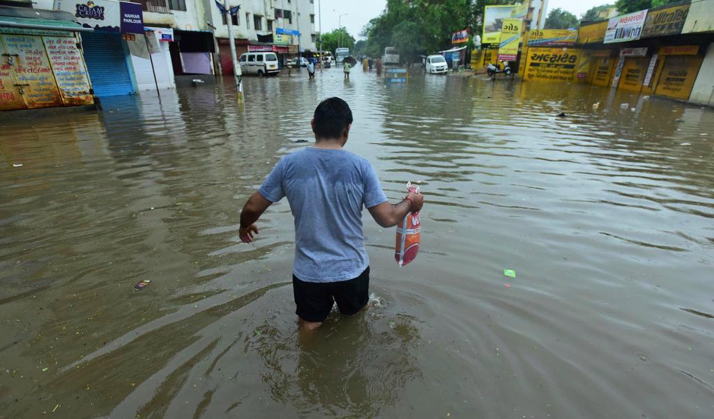 
En man vadar på en översvämmad gata i Ahmadabad i den indiska delstaten Gujarat. Foto: AP/TT                                            