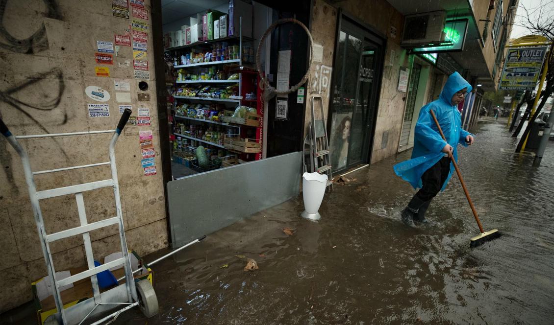 En man försöker få bort vatten från trottoaren utanför sin butik i Rom. Bilden är från i torsdags. Foto: Massimo Percossi/Ansa/AP/TT