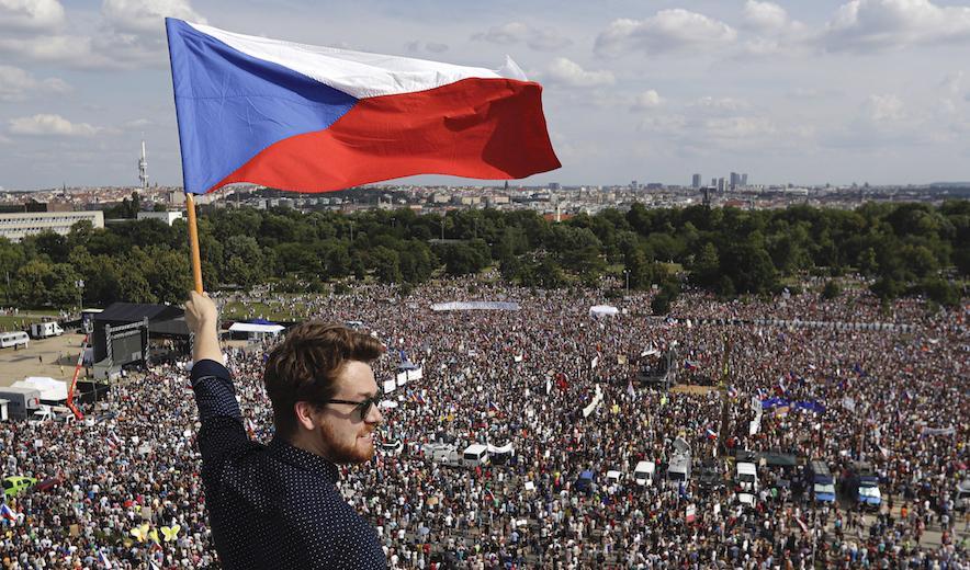 En man håller i den tjeckiska flaggan. I bakgrunden syns de tusentals demonstranter som samlats i Tjeckiens huvudstad Prag för att kräva premiärministerns avgång. Foto: Petr David Josek/AP/TT