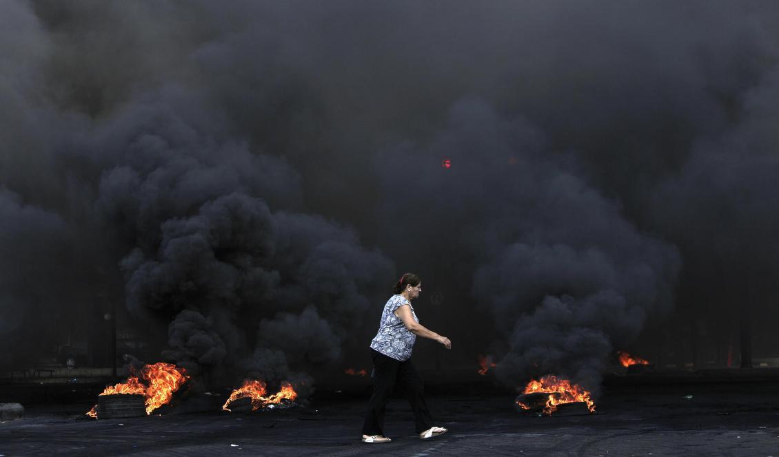 En kvinna går förbi brinnande bildäck under protesterna i Beirut. Foto: Hassan Ammar/AP/TT