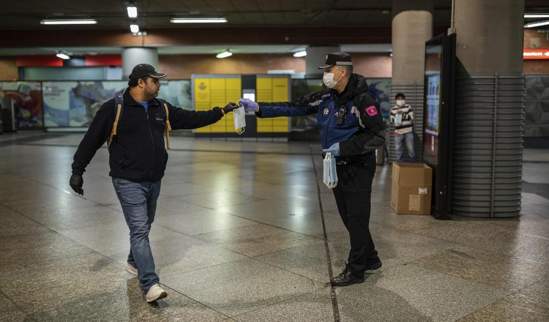 En morgonpendlare tar emot ett andningsskydd av en polisman vid tågstationen Atocha i Madrid under måndagsmorgonen. Foto: Bernat Armangue/AP/TT