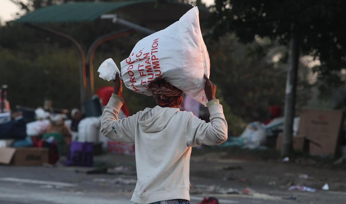 En man bär iväg med en stulen rissäck i Mobeni, söder om Durban. Militär och polis försöker stävja våldet och plundringen som startade i Sydafrika för en dryg vecka sedan. Foto: AP/TT
