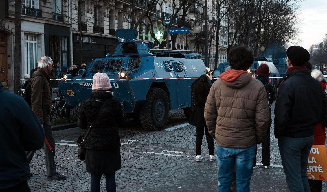 Människor i Paris står framför ett av polisens militärfordon. Foto: Thibault Camus/AP/TT