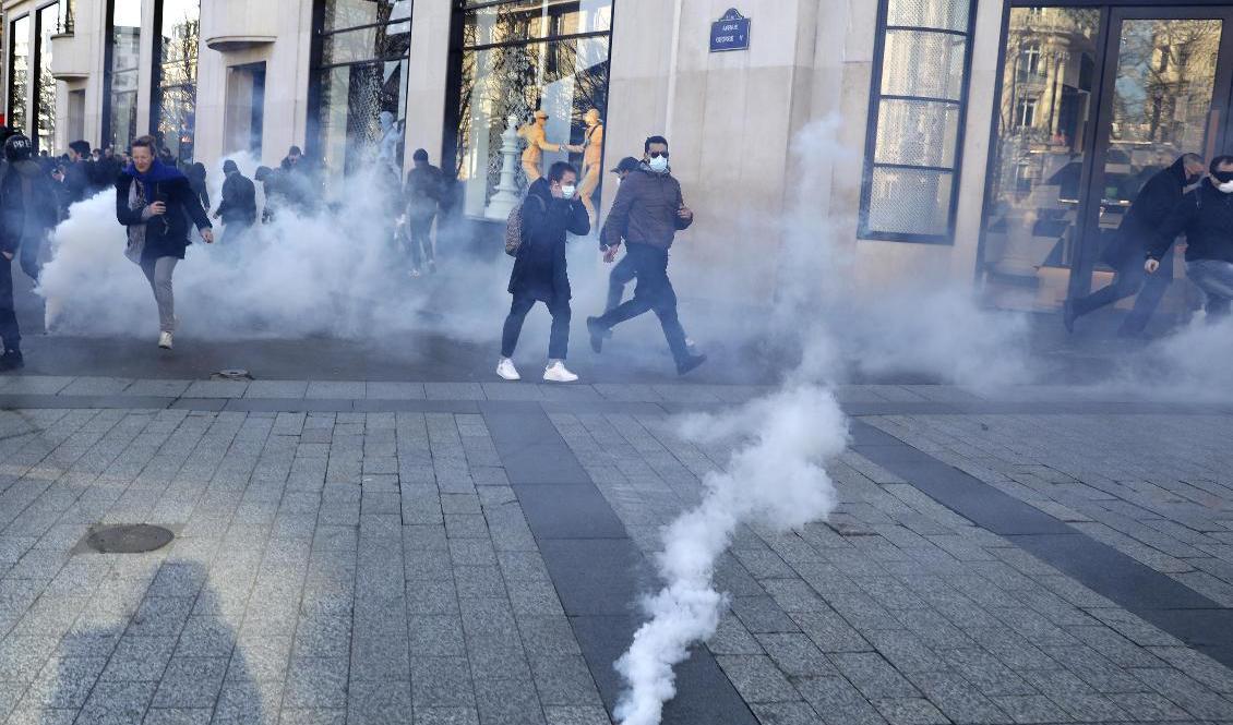 En tårgasgranat landar på Paris paradgata Champs-Elysees där en mix av regeringskritiska demonstranter samlats för att protestera mot bland annat coronarestriktionerna. Foto: Adrienne Surprenant/AP/TT