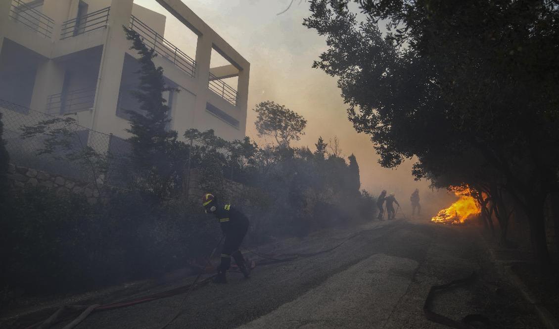 Brandmän försöker släcka i närheten av ett hus i Penteli-bergen. Foto: Thanassis Stavrakis/AP/TT