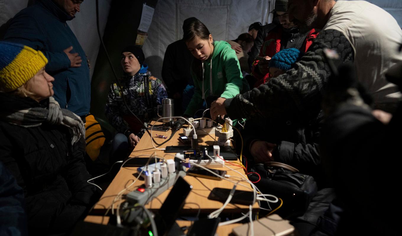 Chersonbor laddar sina telefoner och värmer sig i ett av många tält som myndigheterna har rest. Foto: Evgeniy Maloletka/AP/TT