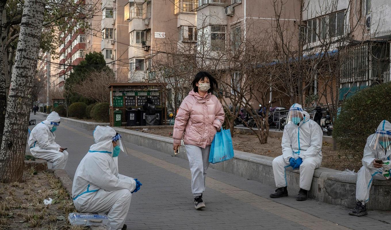 En person promenerar bland sanitetspersonal i Peking i Kina den 6 december 2022. Foto: Kevin Frayer/Getty Images