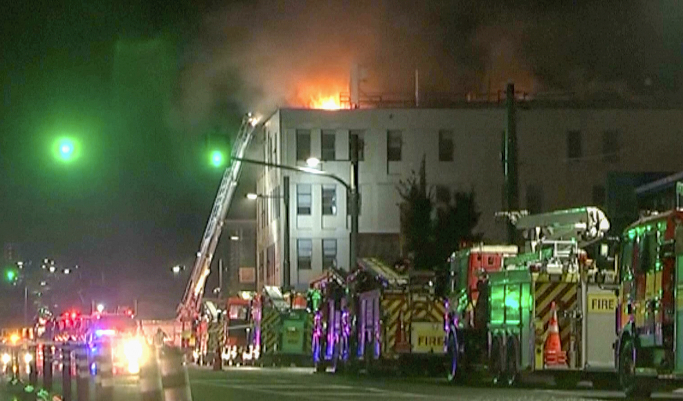Lågor syns slå upp genom taket på byggnaden, därifrån flera personer fick räddas via stegbil. Bilden är tagen från ett videoklipp. Foto: NewsHub/AP/TT