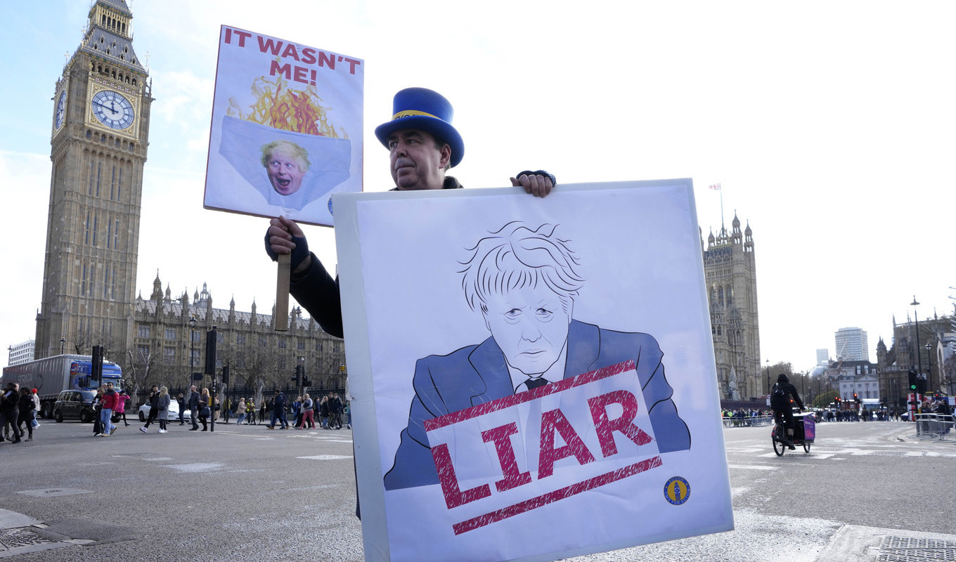 En demonstrant håller upp ett plakat utanför parlamentet i London, där tidigare premiärministern Boris Johnson fick svara på anklagelser om att han vilselett parlamentet angående sin kännedom om brott mot pandemilagarna. Arkivbild. Foto: Kirsty Wigglesworth/AP/TT