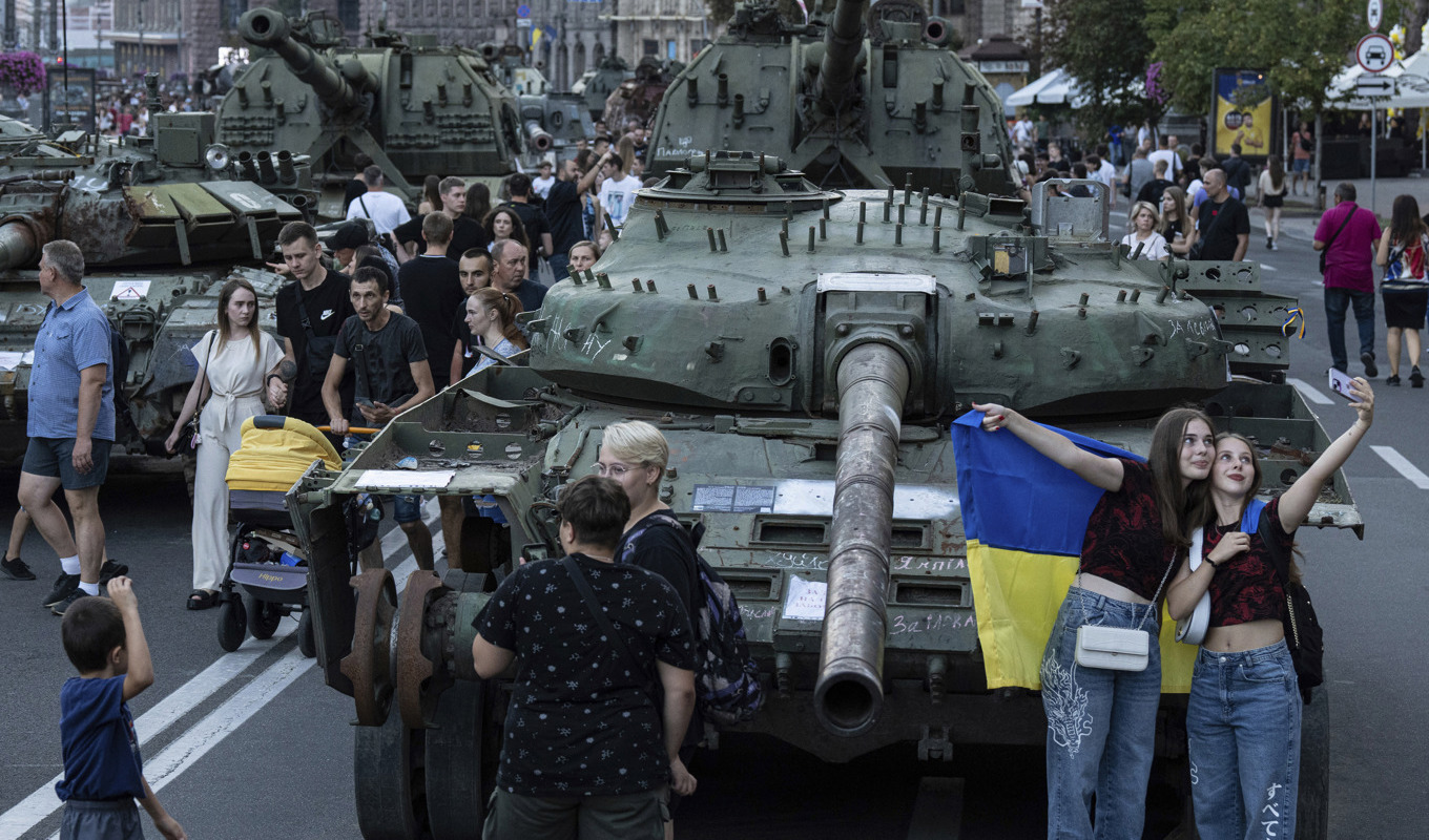 Invånare i Kiev poserar framför en förstörd rysk stridsvagn. Bilden är från i lördags. Foto: Evgeniy Maloletka/AP/TT