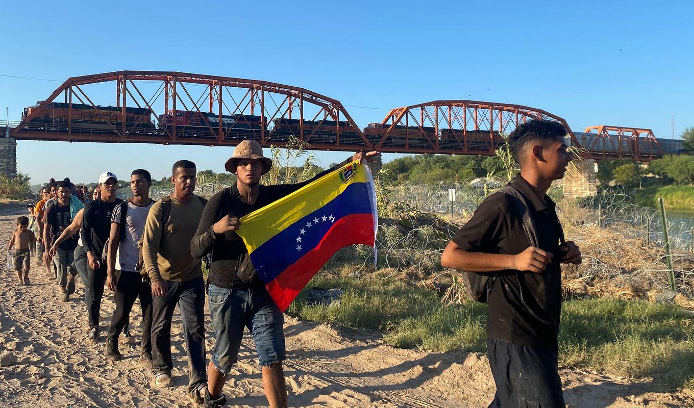 Migranter med den venezuelanska flaggan passerar in i USA från Mexiko den 23 september i hopp om att få stanna i landet. Foto: PAULA RAMON / AFP via Getty Images