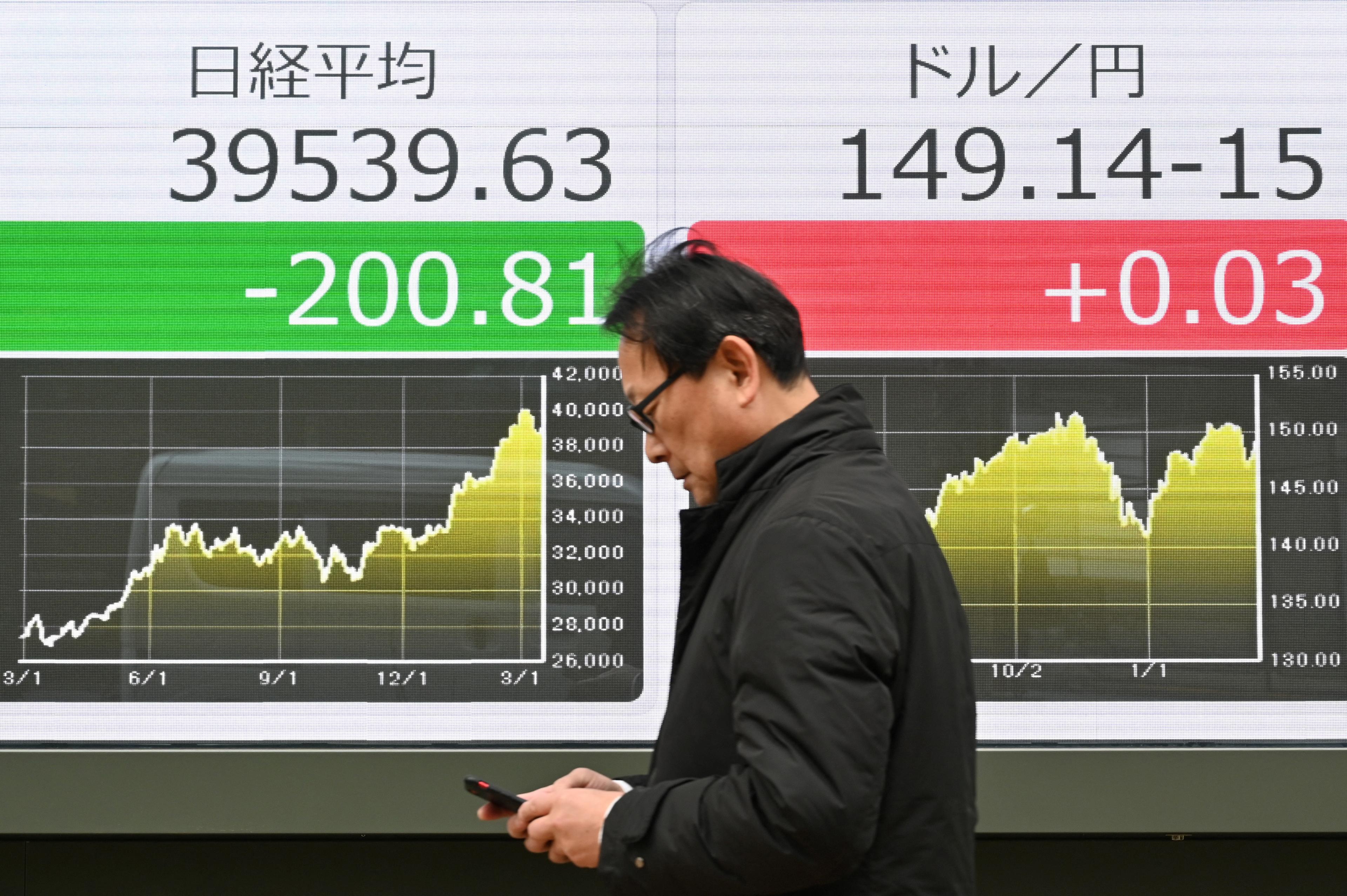 En man går förbi en elektronisk tavla som visar aktiekursen på Tokyobörsen och kursen för den japanska yenen gentemot den amerikanska dollarn längs en gata i Tokyo den 19 mars. (Foto: Kazuhiro Nogi/AFP via Getty Images