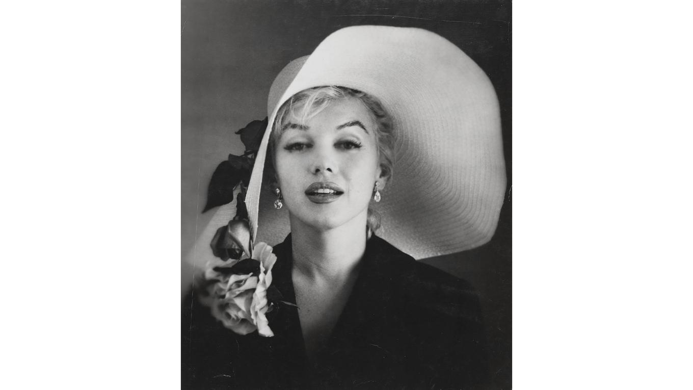 Ett svartvitt fotografi av Marilyn Monroe, iförd en stor vit stråhatt med rosor, taget av Carl Perutz 1958. Fotot har ett uppskattat pris på 700–900 dollar. Enligt samstämmiga uppgifter var det DiMaggio som såg till att Marilyns grav alltid pryddes av färska röda rosor – ett löfte som han höll i över 20 år, fram till sin egen död, genom att låta en florist leverera dem tre gånger i veckan. Foto: Christie’s Images LTD. 2025