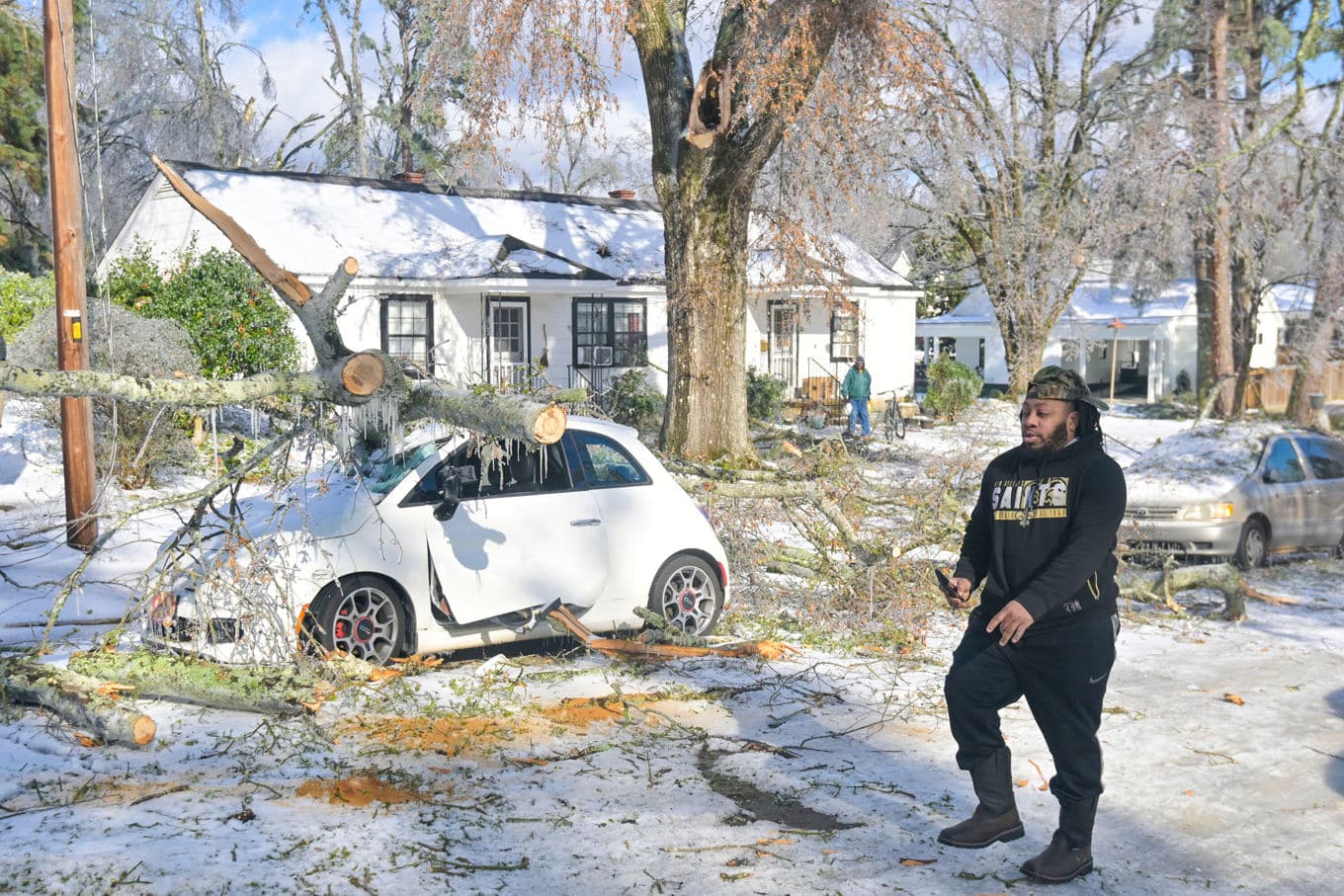 En man går förbi en bil som skadats av ett träd i Oxford i delstaten Mississippi under snöstormen. Foto: Bruce Newman /AP/TT