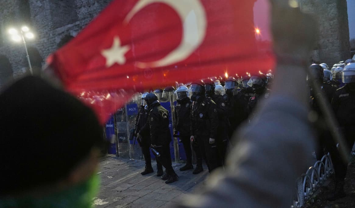En demonstrant håller en turkisk flagga medan kravallpolis vaktar under en protest efter att Istanbuls borgmästare Ekrem Imamoglu greps i mars i fjol. Foto: Francisco Seco/AP/TT. Arkivbild