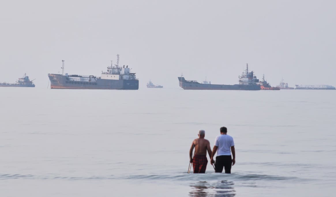 Två män vadar i vattnet i Hormuzsundet, med fartyg för ankar i bakgrunden, utanför Bandar Abbas i Iran. Foto: Razieh Poudat/AP/TT