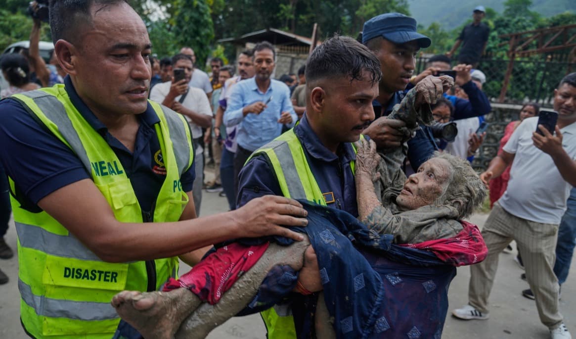 Räddningsabetare i Nepals distrikt Nuwakot för en drabbad kvinna till säkerhet. Foto: Niranjan Shrestha/AP/TT