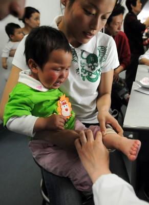 En mor visar upp möjliga symptom på hand- fot- och munsjuka, även kallat "höstblåsor" på sitt barn. Över hundra nya fall rapporteras dagligen i Peking och sjukdomsspridningen kommer troligen nå sin topp under juni. (Foto: STR/ AFP)
