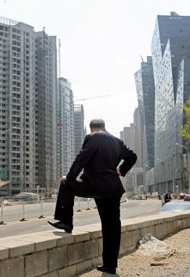 En kinesisk man står framför några kontors- och lägenhetsbyggnader i Peking i april 2007, då fastighetspriserna hade skjutit i höjden. Färsk statistik visar att transaktionsvolymerna per vecka har sjunkit på Kinas bostandsmarknad. (Foto: Teh Eng Koon/ AFP) 