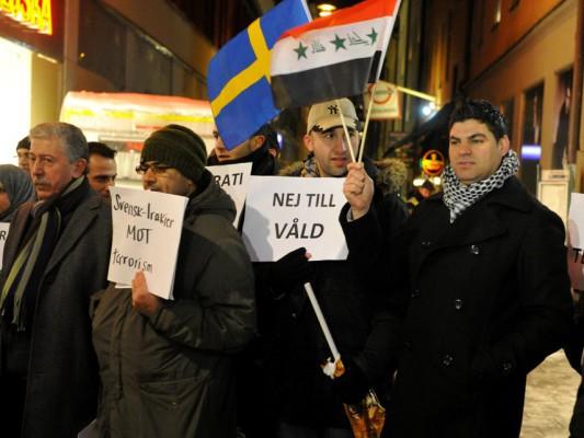 Protesterande håller upp en svensk flagga jämte en irakisk i en liten demonstration mot våld på platsen för självmordsbomben i hörnet av Bryggaregatan och Drottninggatan den 13 december 2010. (Foto: Bertil Ericson/ AFP)